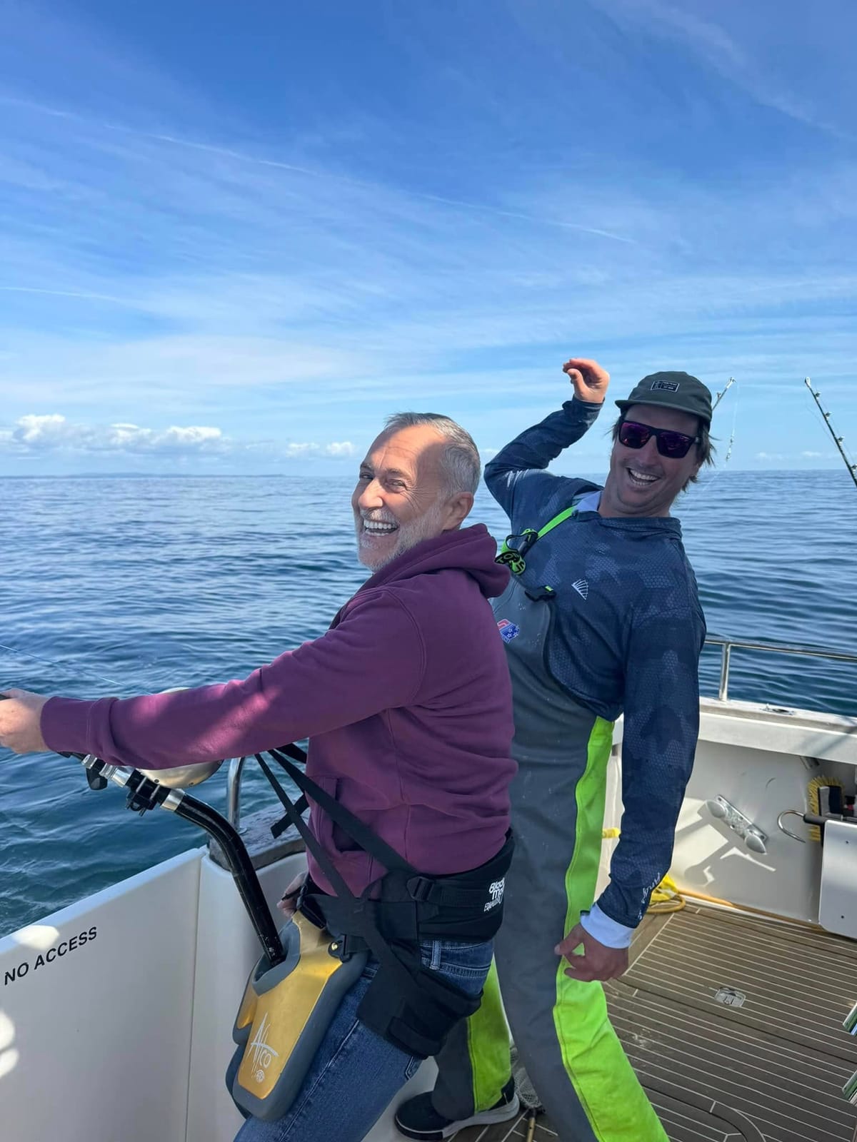 Two anglers laughing on the deck of Dreamcatcher, one strapped into a fighting harness
