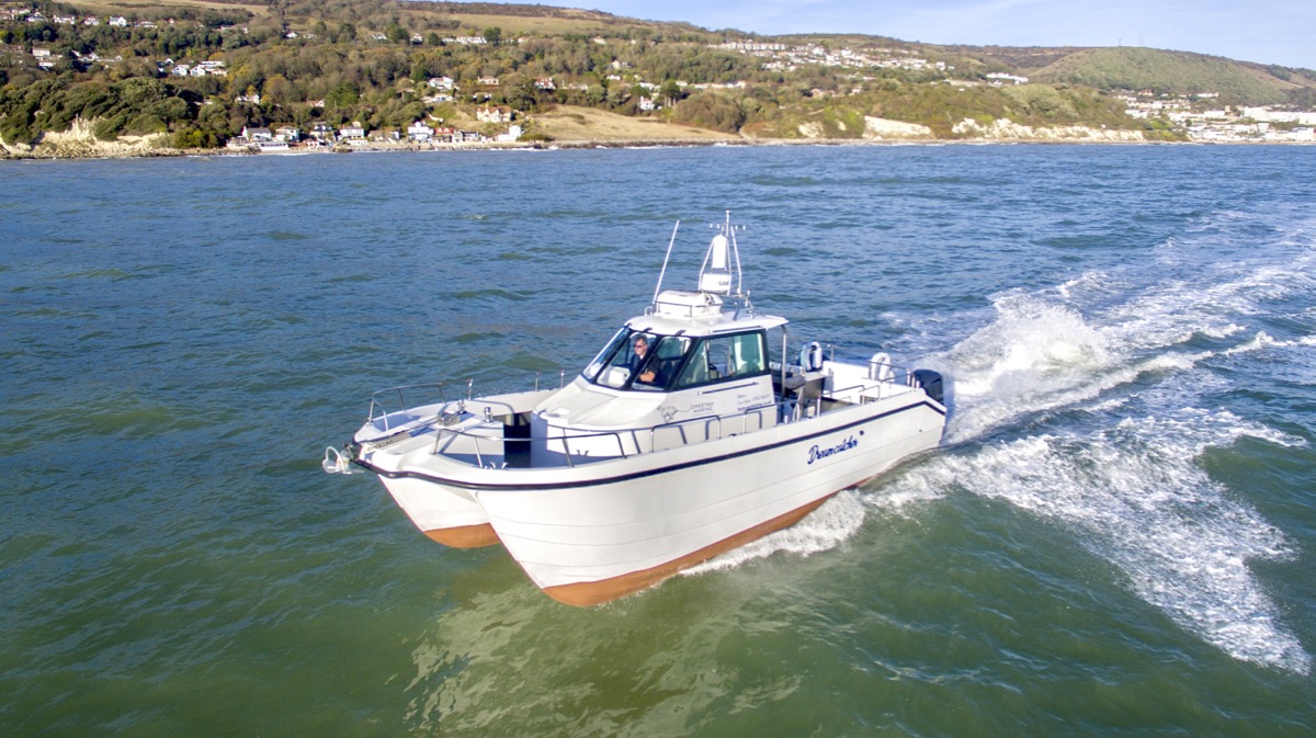 Dreamcatcher, a white 9.7 metre Cheetah catamaran, running at speed along the coast