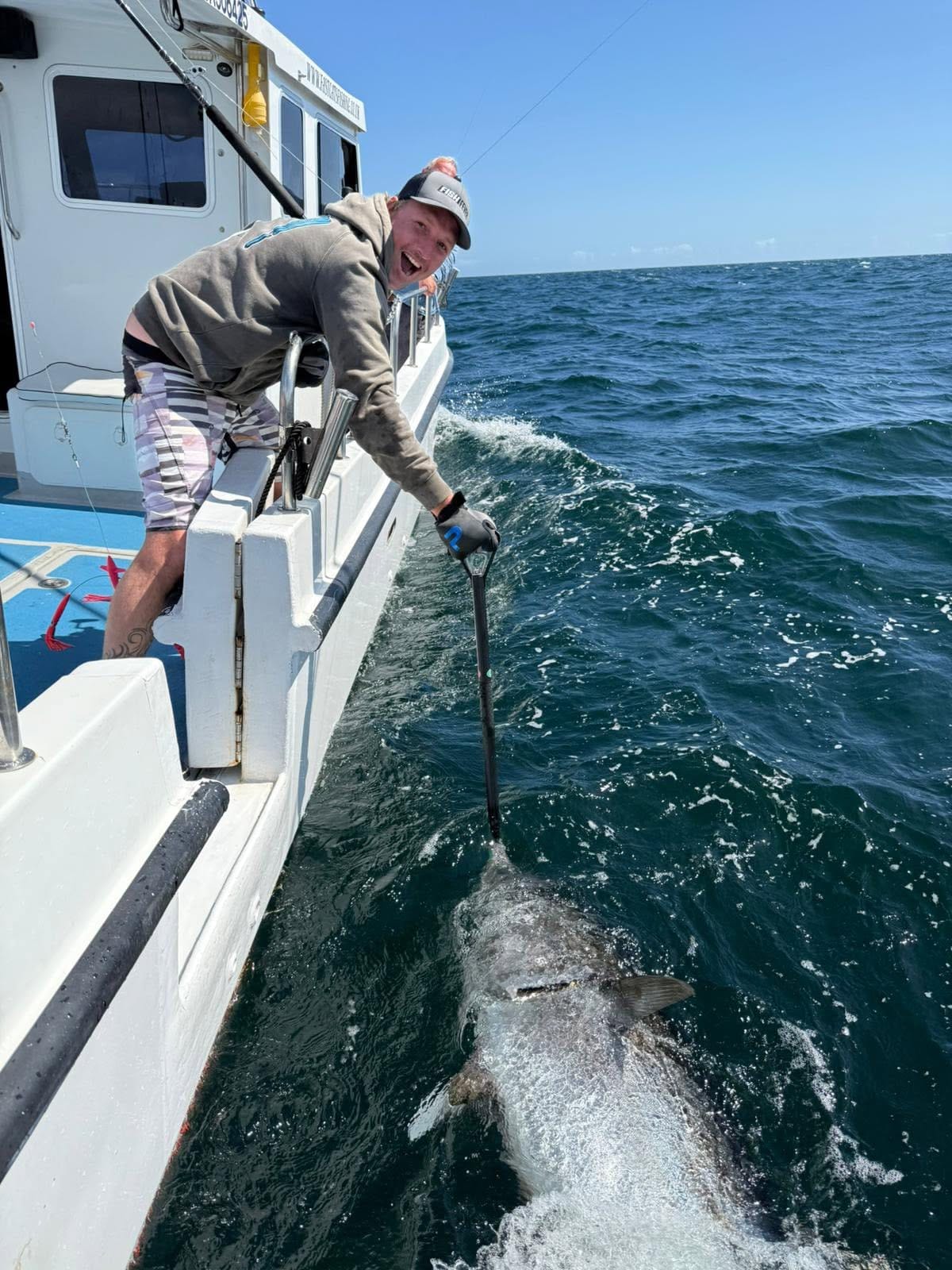 A laughing angler leans over the gunwale holding a big bluefin on a lip grip