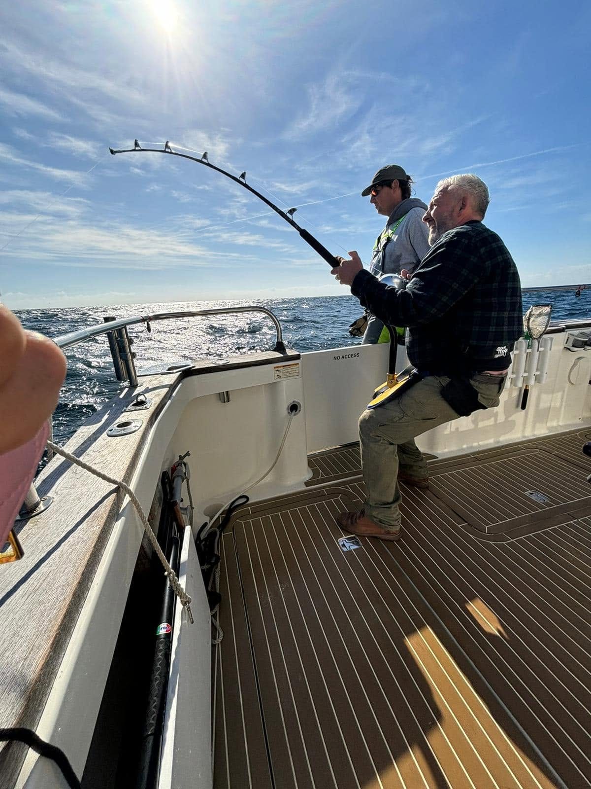 An angler in a fighting harness leans back into a bent rod with the deckhand beside him